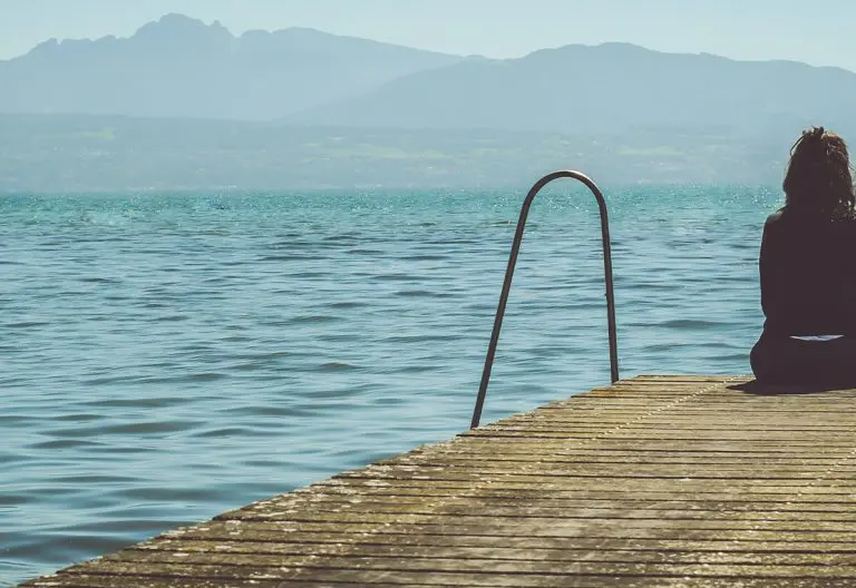 a woman sitting on a dock looking out at the water.