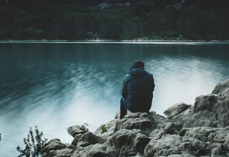 a person sitting on top of a rock next to a body of water.