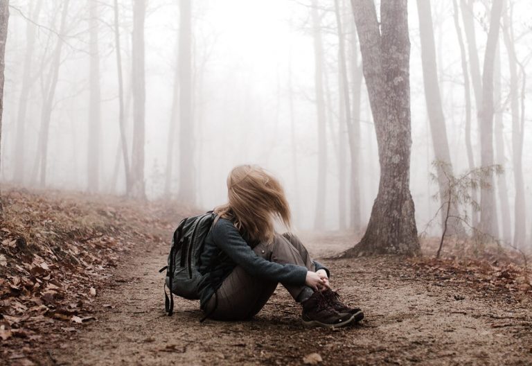 a woman sitting on a trail in a foggy forest.