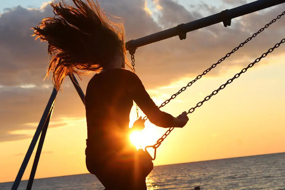 Woman happily swaying on a swing set near a sunset