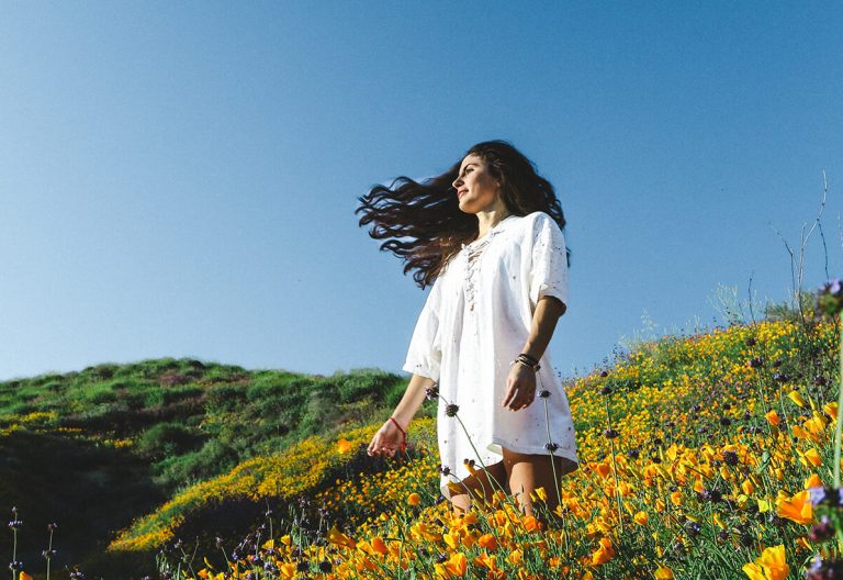 a woman walking through a field of flowers.