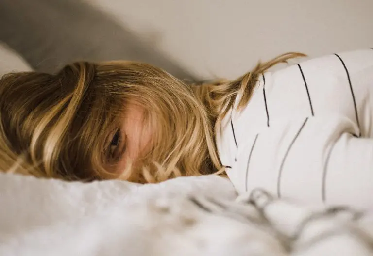 a woman laying on top of a bed under a blanket.