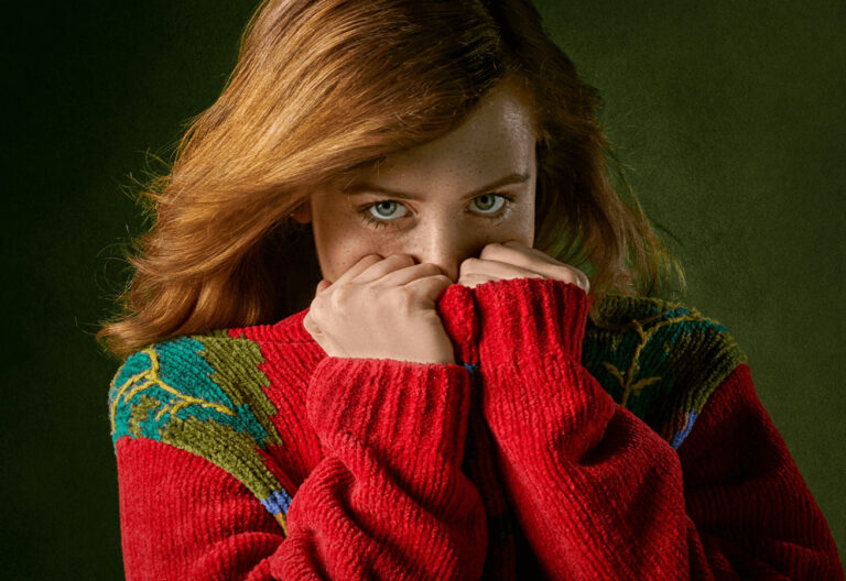 a woman in a red sweater covers her face with her hands.