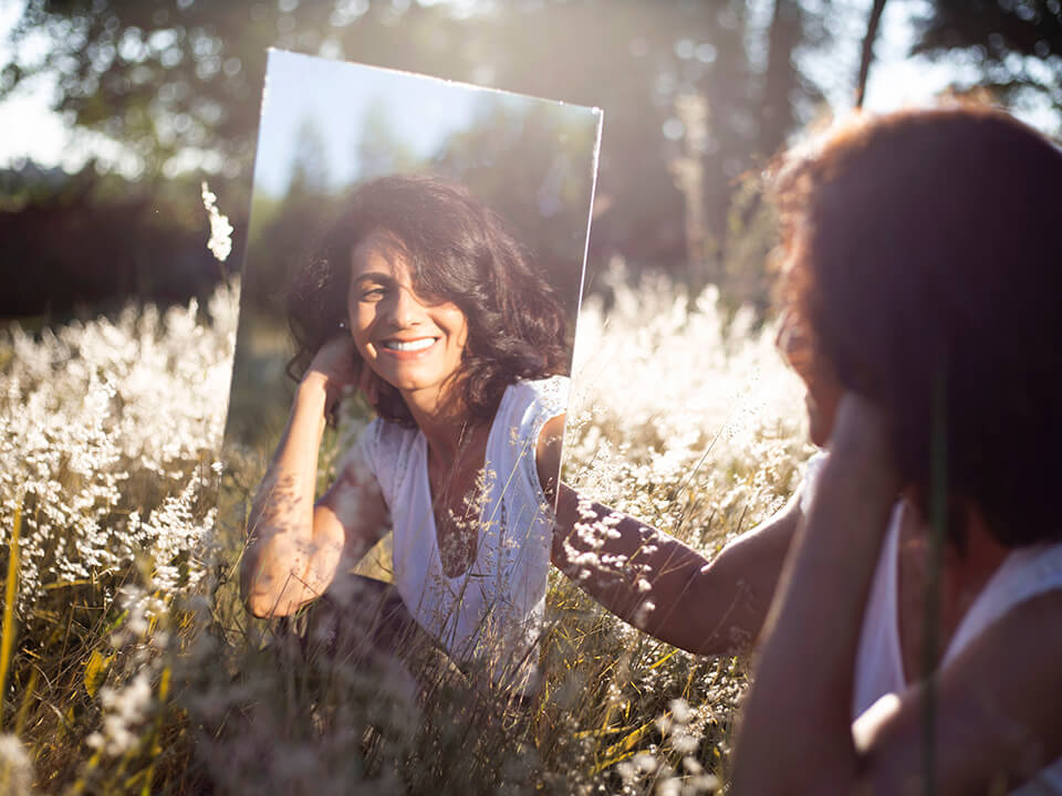 Woman looking at herself in the mirror in a field