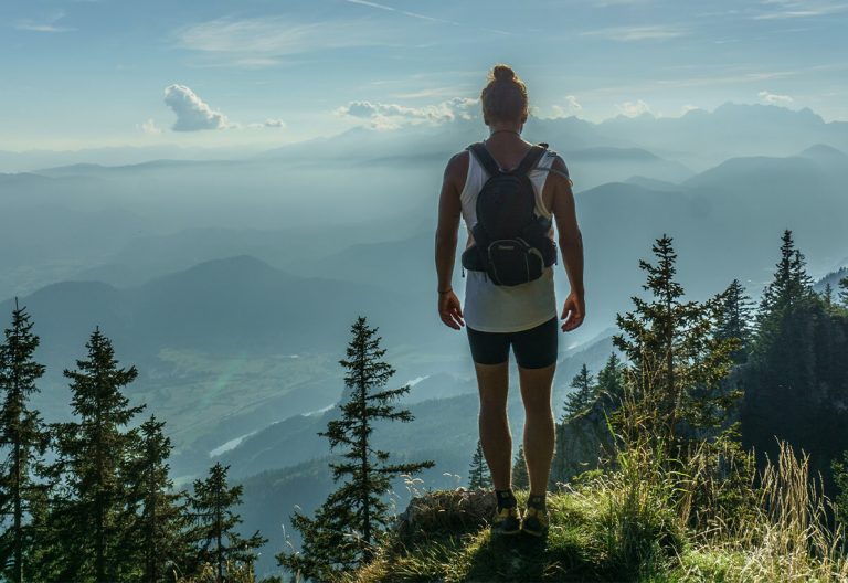 a woman standing on top of a lush green hillside.