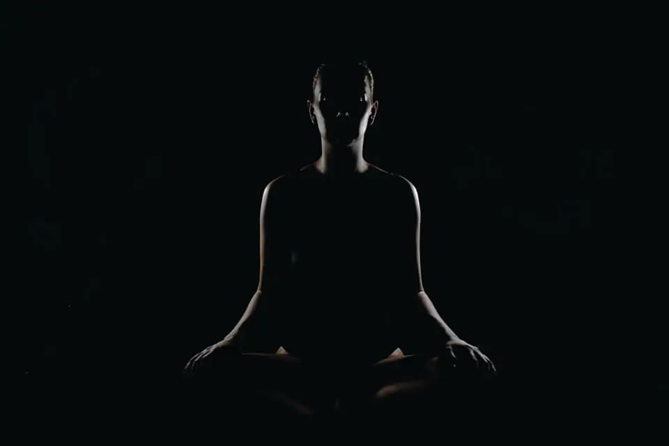 Woman sitting in the dark, in a lotus pose, meditating