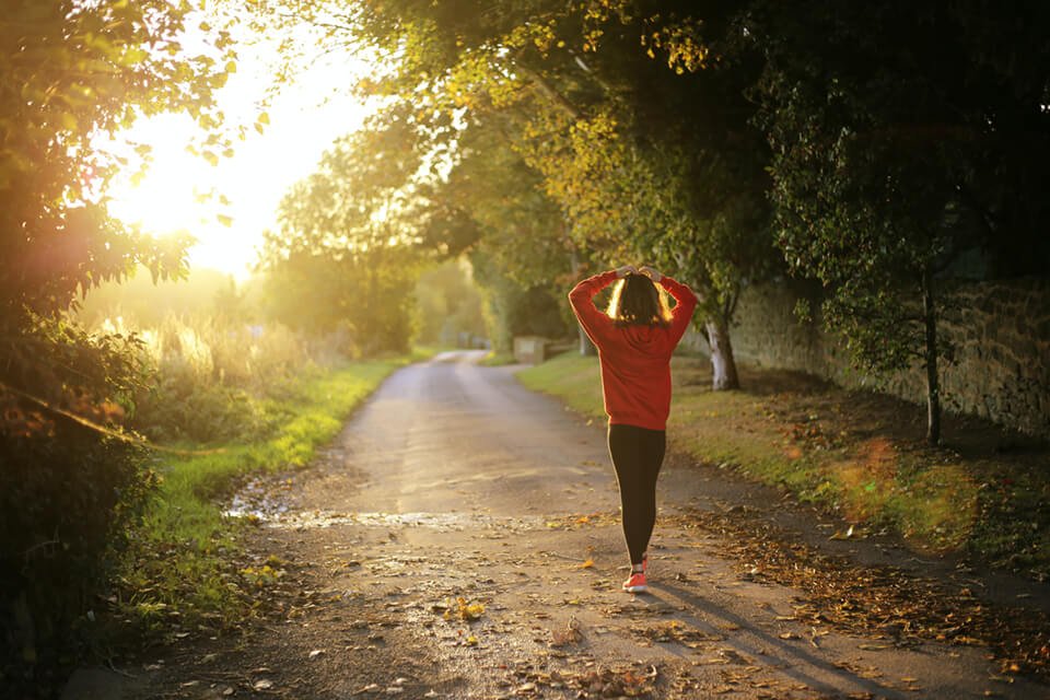 Woman walking outside as the sun sets, with her hand over her head