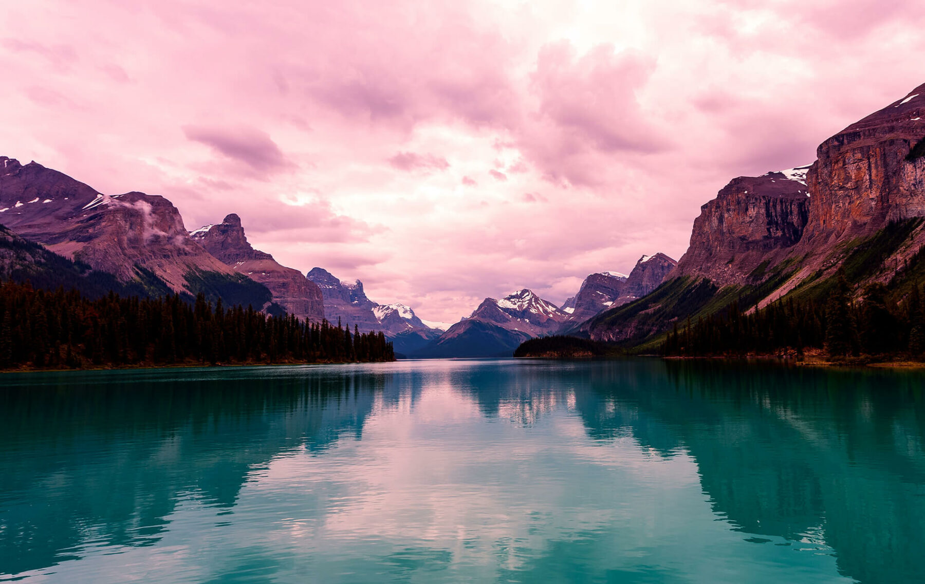 a lake surrounded by mountains under a cloudy sky.