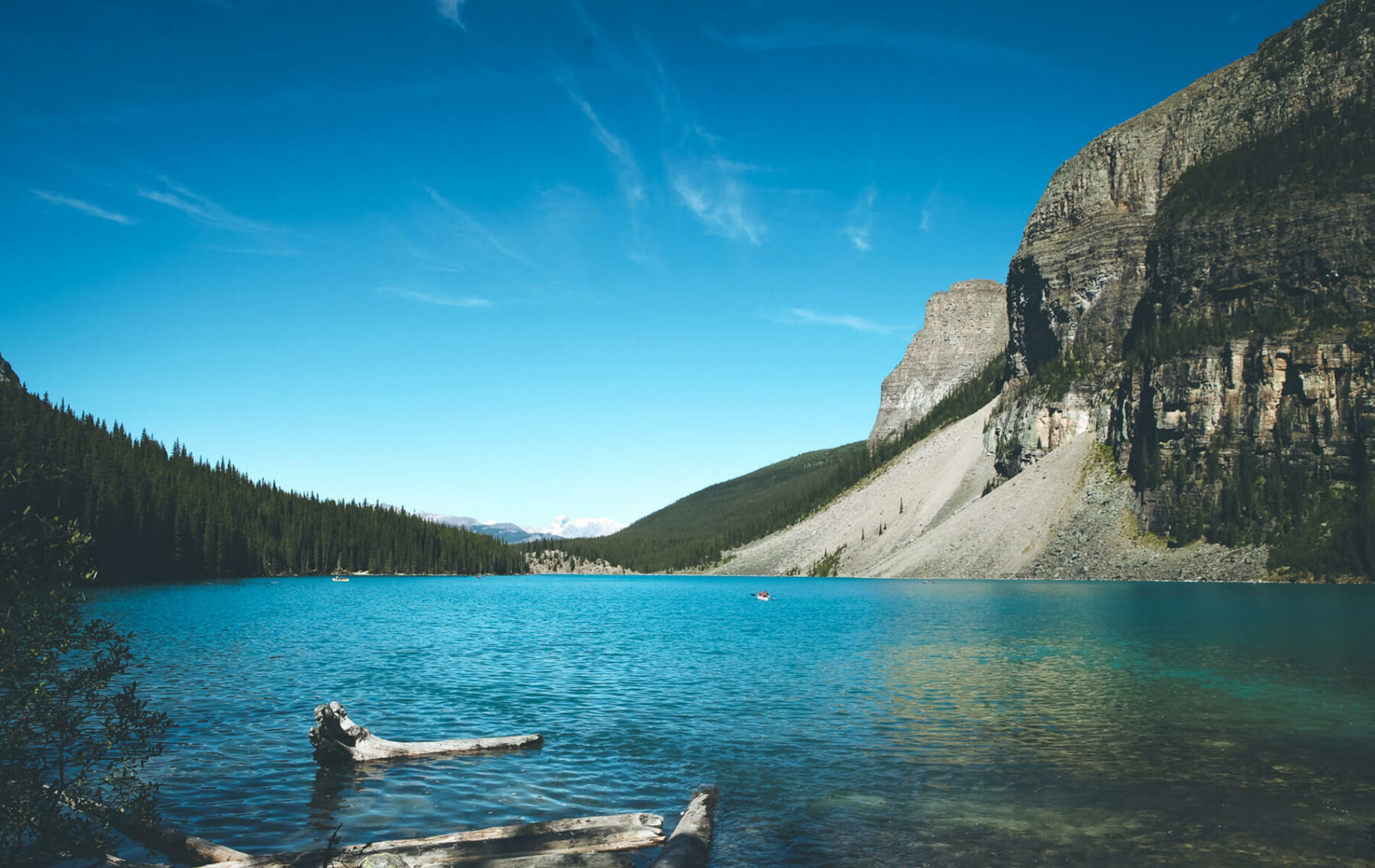 a lake surrounded by mountains and trees on a sunny day.