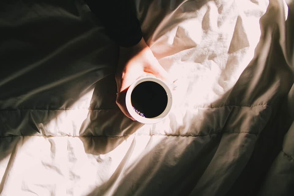 Cup of coffee held out over bed