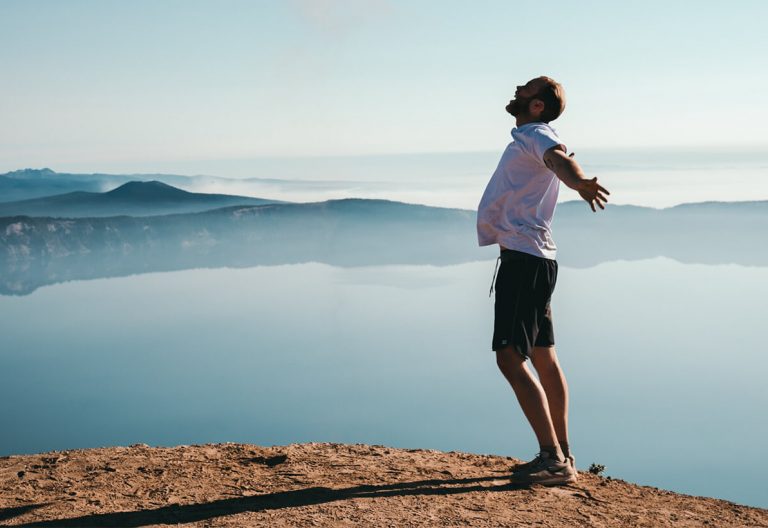 a man standing on top of a mountain next to a lake.