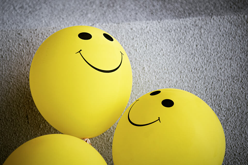 Three bright yellow balloons with smiley faces on them