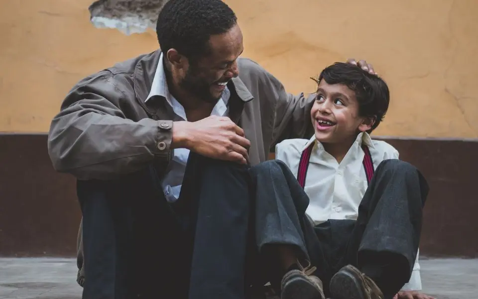 a man sitting next to a little boy on the ground.