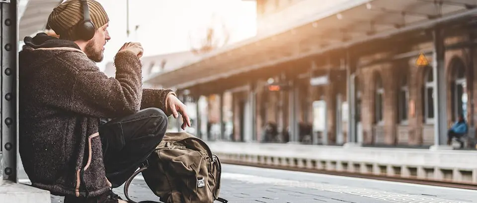 a man sitting on a train platform with a backpack.