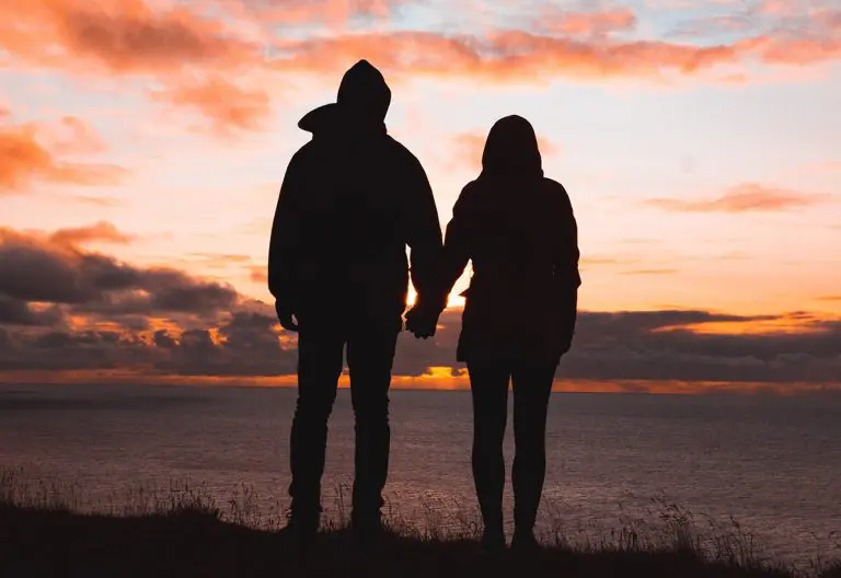 a man and a woman holding hands as the sun sets.