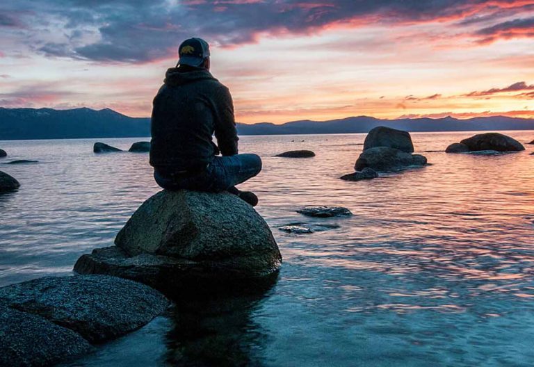 a person sitting on top of a rock near the ocean.