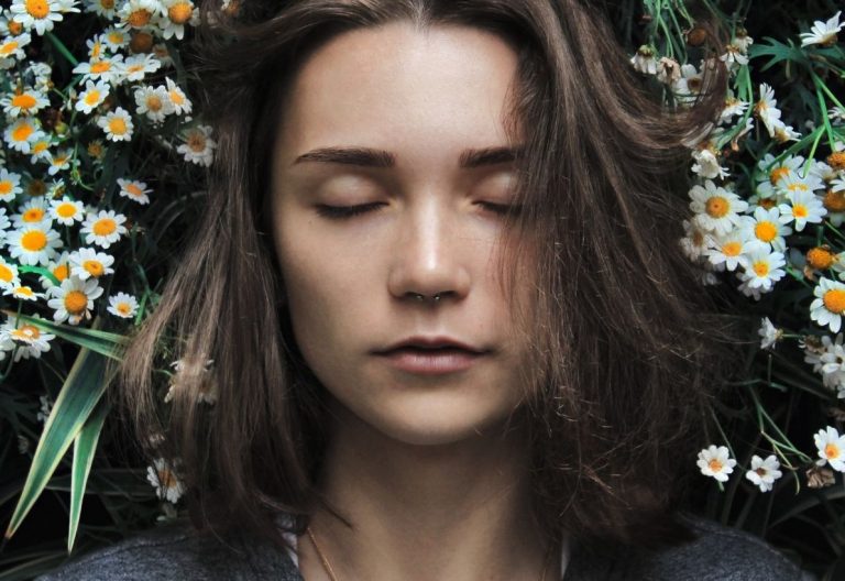 a woman with her eyes closed standing in front of flowers.