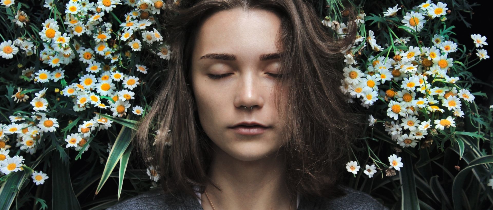 a woman with her eyes closed standing in front of flowers.