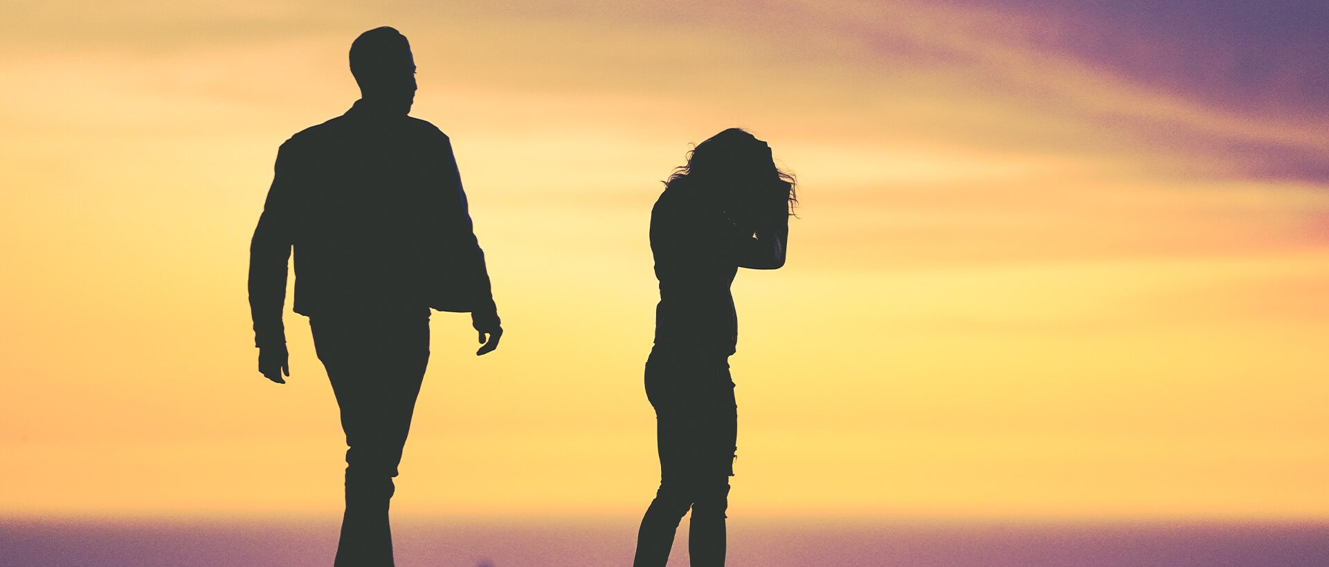 a man and a woman standing on a beach at sunset.