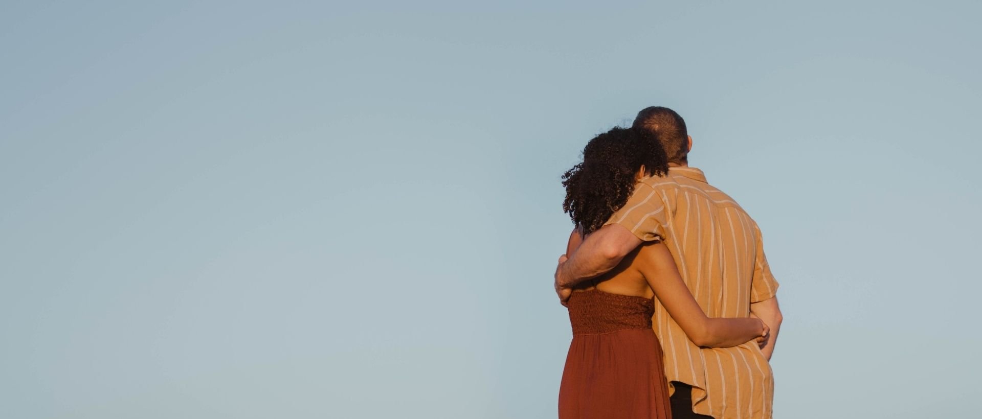 a man and a woman standing back to back with their arms around each other.