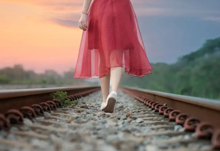 a woman in a red dress walking on a train track.