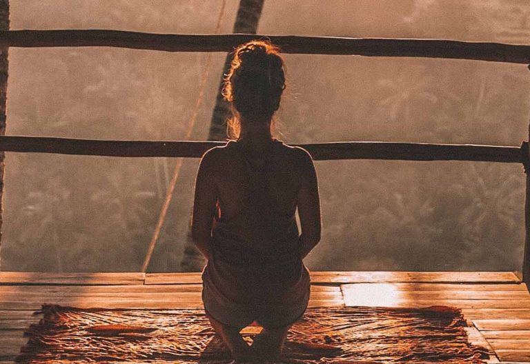 a woman sitting on a wooden platform in a hut.