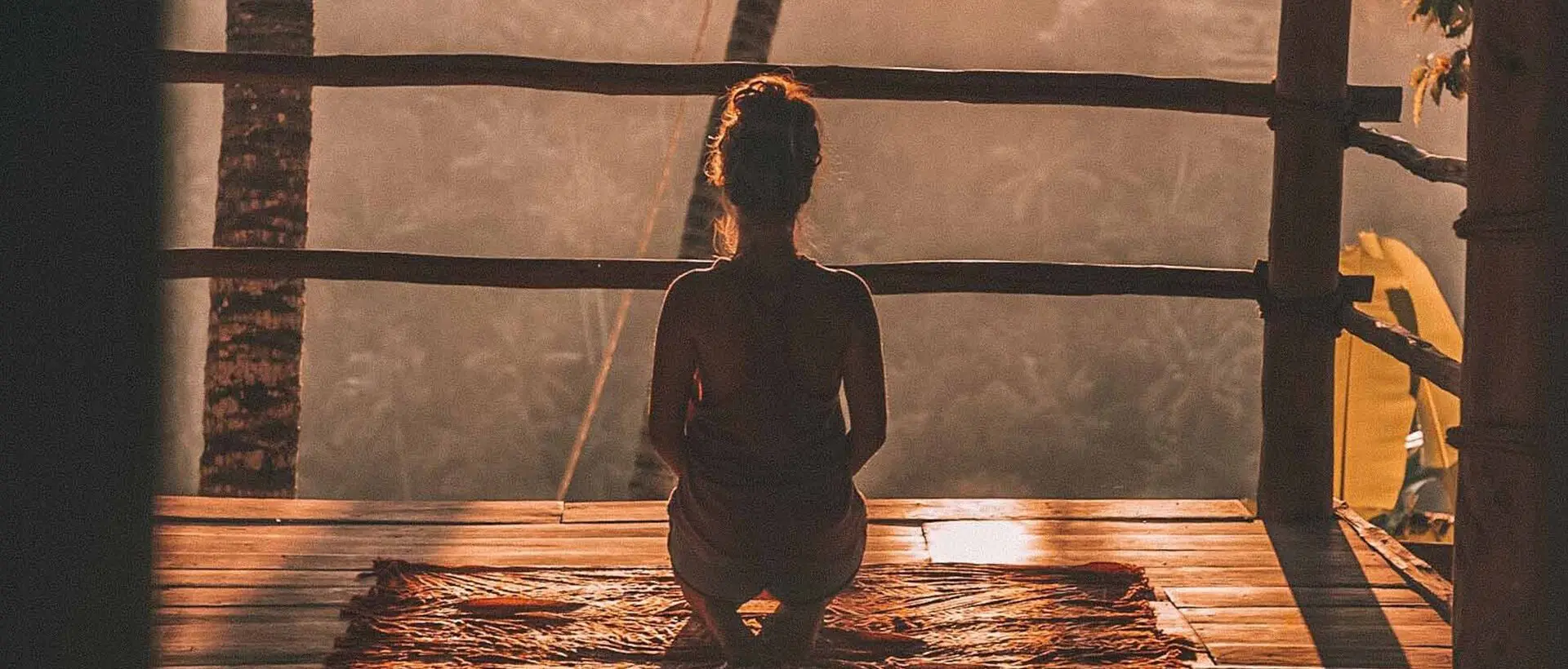 a woman sitting on a wooden platform in a hut.