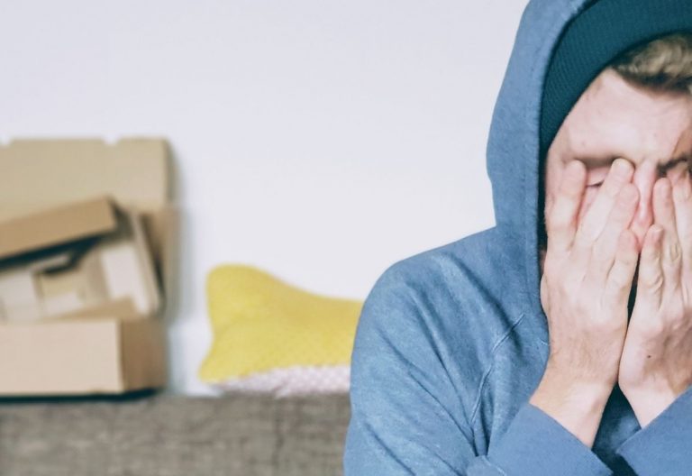 a man sitting on a couch covering his face with his hands.