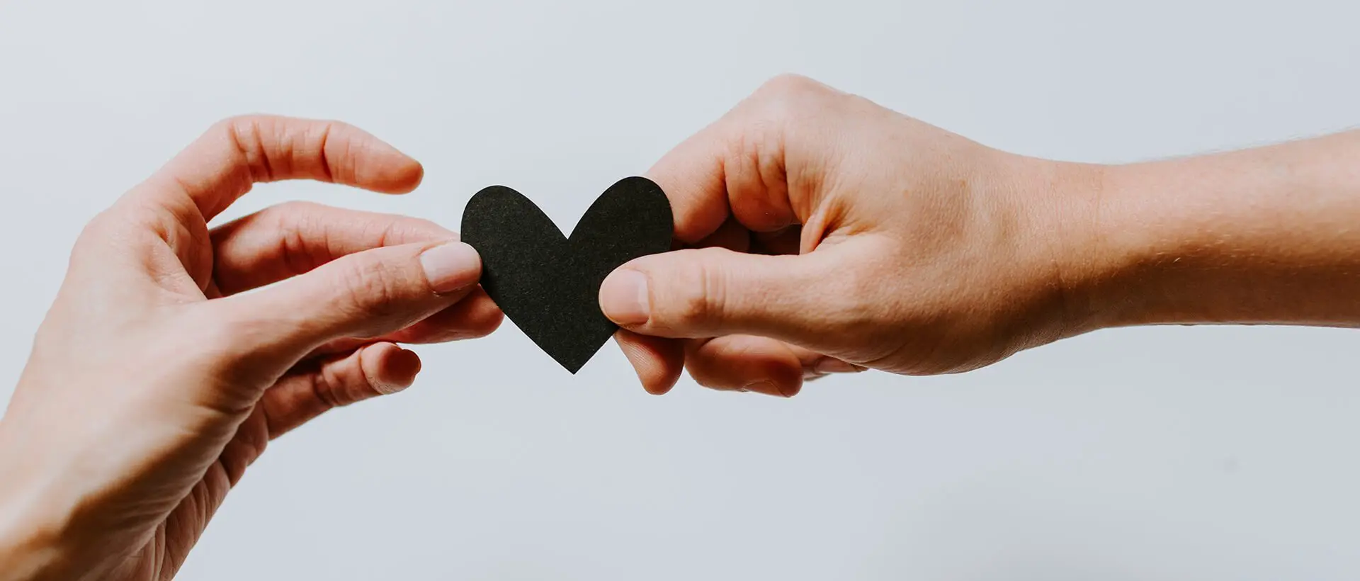 two hands holding a piece of paper in the shape of a heart.