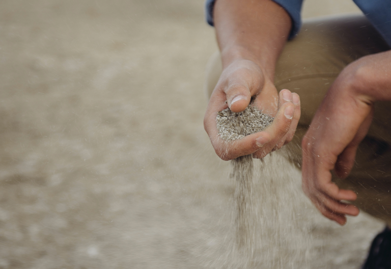 a man kneeling down holding a handful of sand.