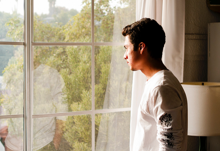 a man looking out of a window at a tree.